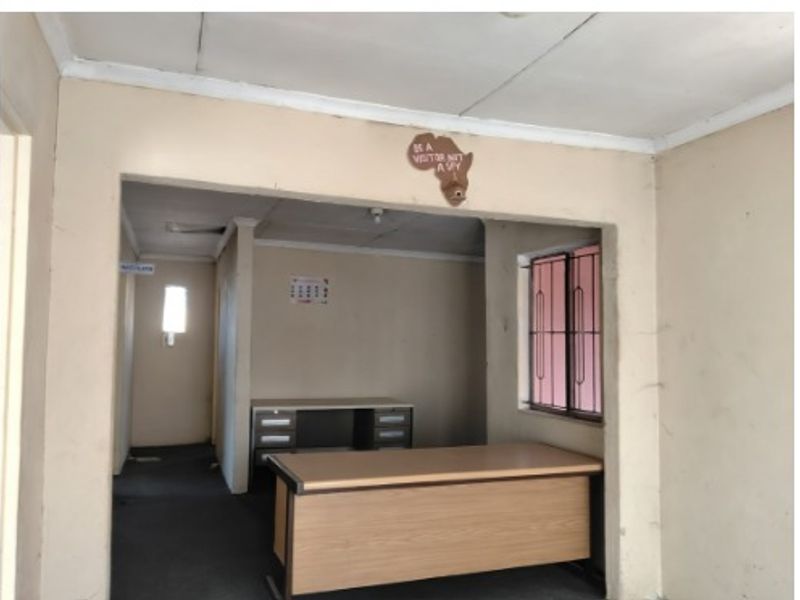 An interior view of a basic office or utility space featuring simple wall finishes, a window with security bars, and a functional layout.