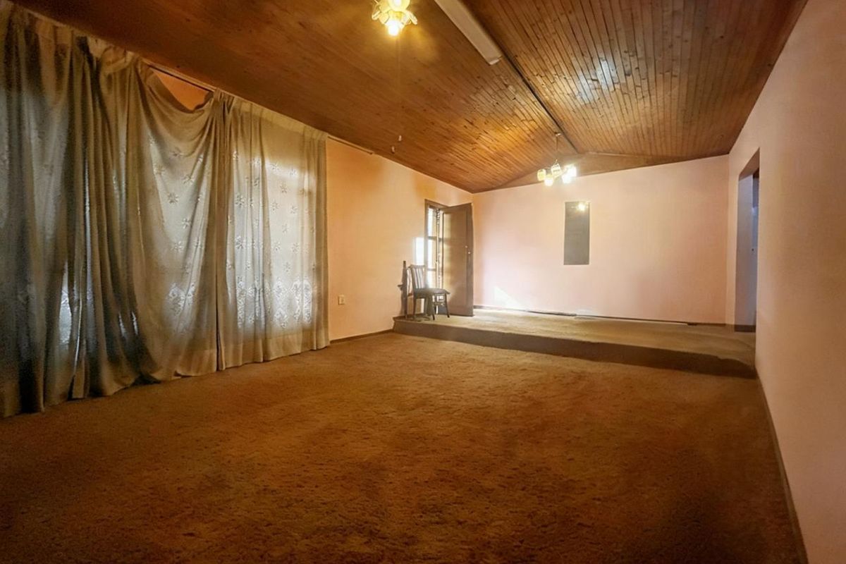 Spacious living area featuring a unique raised platform, timber-clad vaulted ceiling, and neutral wall finishes, offering a blank canvas for renovation.