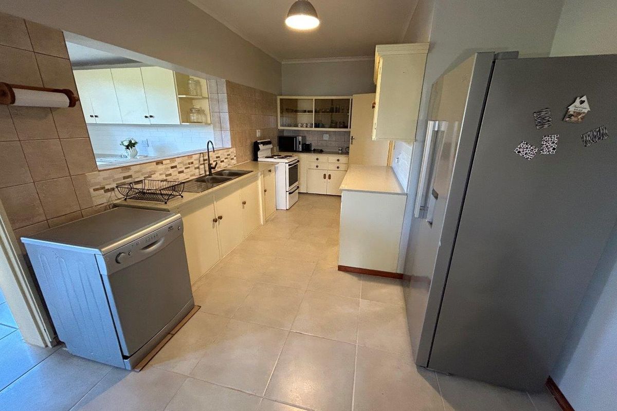 A functional kitchen featuring tiled flooring, built-in cabinetry, a double sink, and a pass-through window connecting to an adjacent space.