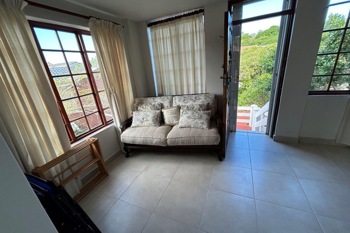 A bright living area featuring tiled flooring, timber-framed windows, and direct access to an outdoor balcony area.