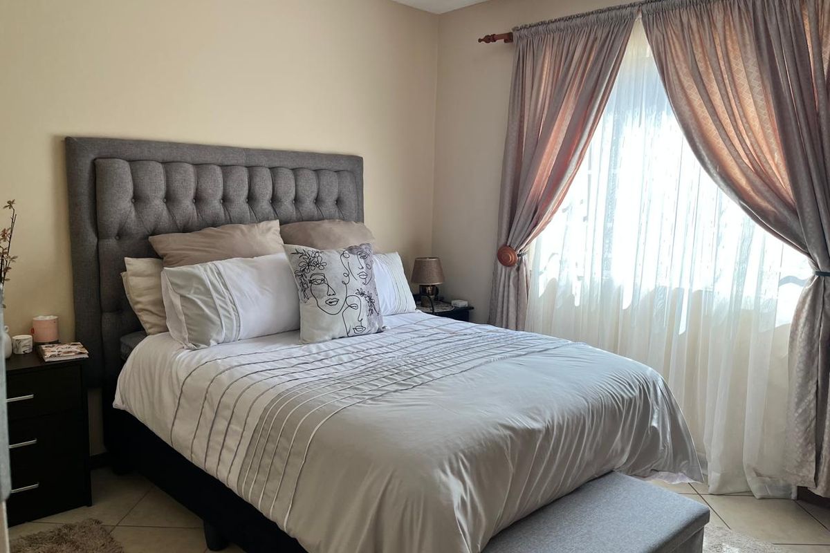 A well-maintained bedroom featuring neutral wall tones, tiled flooring, and a window dressed with classic curtain hardware.