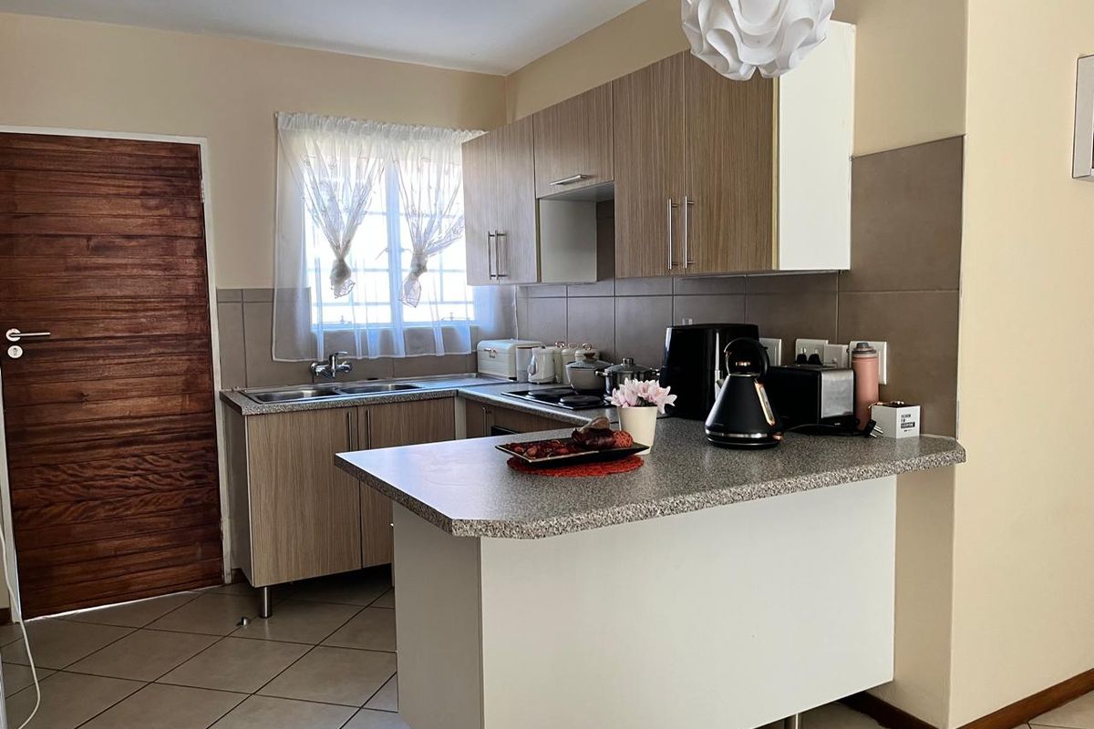 A functional kitchen featuring wood-look cabinetry, a breakfast nook, tiled flooring, and a double sink with a window view.