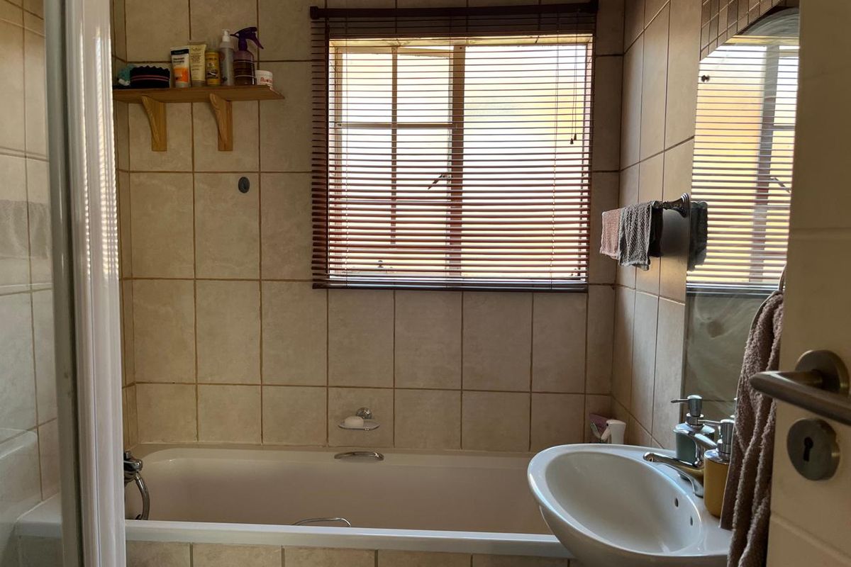 A functional bathroom featuring a built-in bathtub, pedestal basin, and tiled walls, offering a practical layout with natural light from the window.
