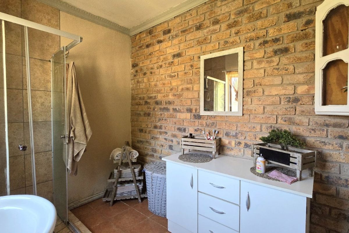 A bathroom featuring a glass-enclosed shower, a freestanding bathtub, and a vanity unit set against a rustic exposed brick feature wall.