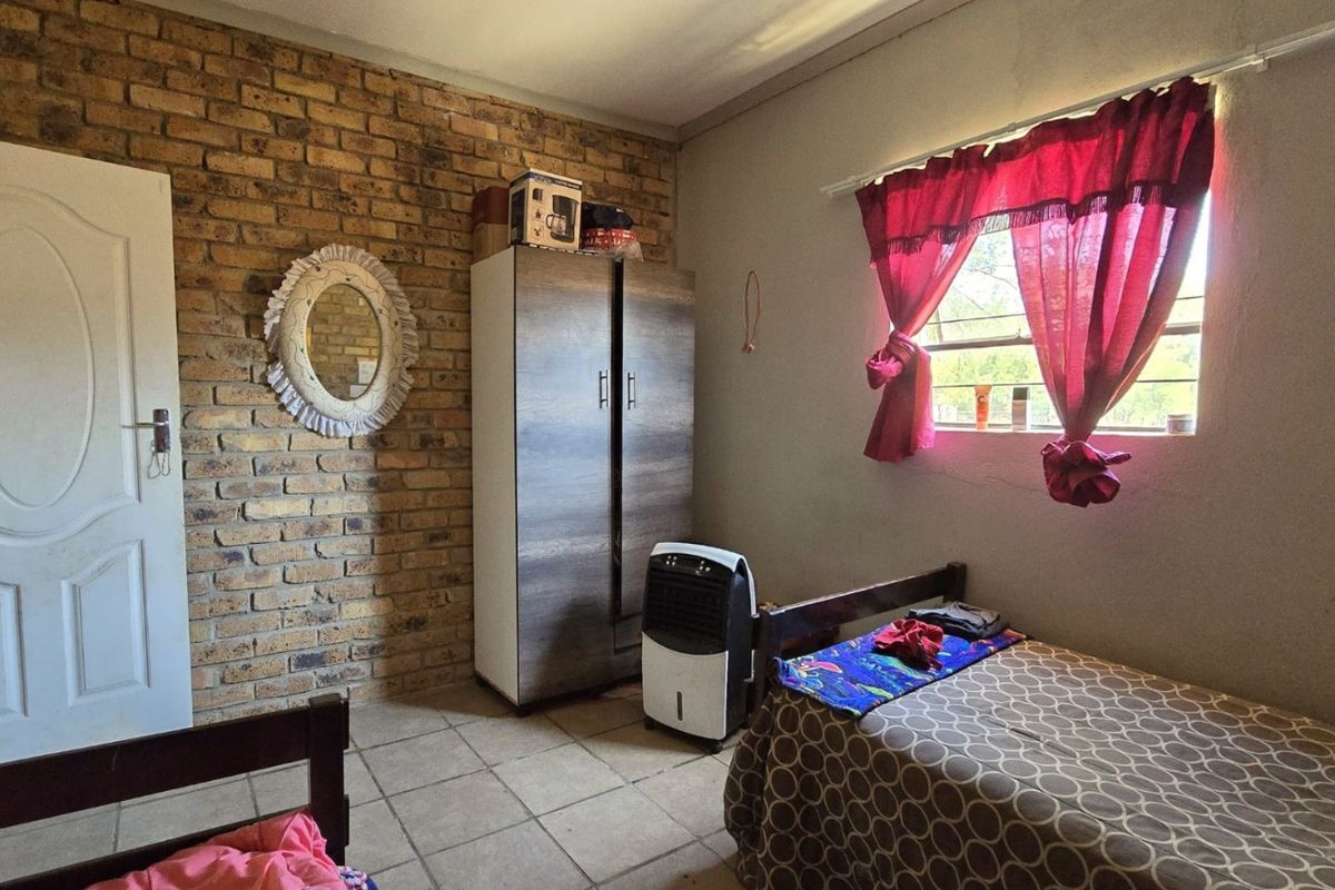 A bedroom featuring a rustic face-brick accent wall, tiled flooring, and a window with natural light.