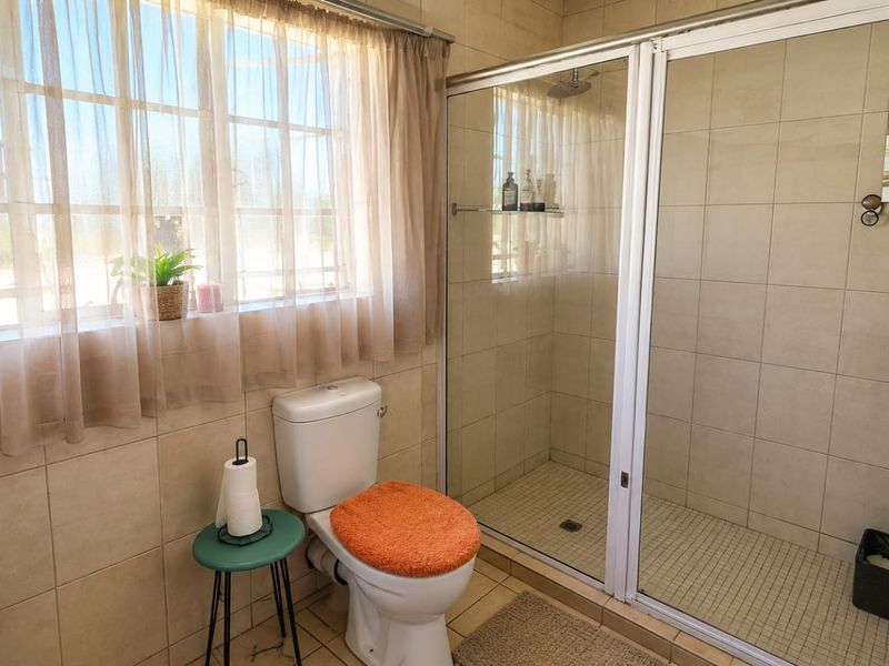 A functional bathroom featuring a glass-enclosed shower, toilet, and washbasin with neutral wall and floor tiling.