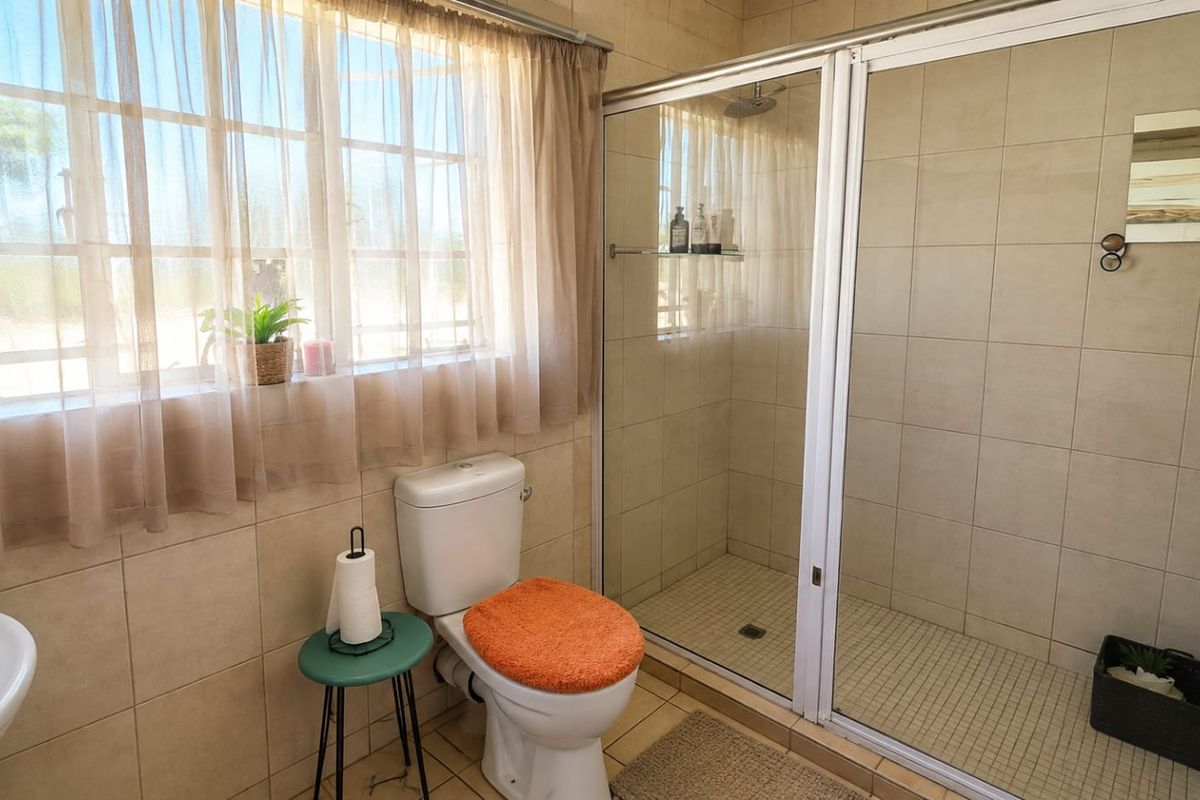 A functional bathroom featuring a glass-enclosed shower, toilet, and washbasin with neutral wall and floor tiling.