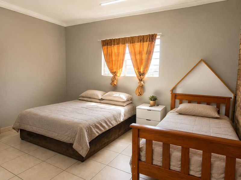 A well-maintained bedroom featuring neutral tiled flooring, a distinctive exposed brick feature wall, and a built-in cupboard for storage.
