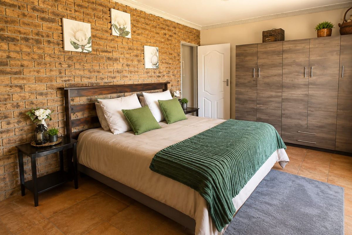 A well-maintained bedroom featuring an exposed brick feature wall, tiled flooring, and a large built-in wardrobe.