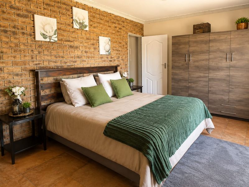 A well-maintained bedroom featuring an exposed brick feature wall, tiled flooring, and a large built-in wardrobe.