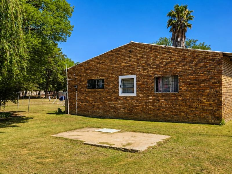 Rear view of a face-brick small holding dwelling featuring security bars on windows and an external concrete slab area.