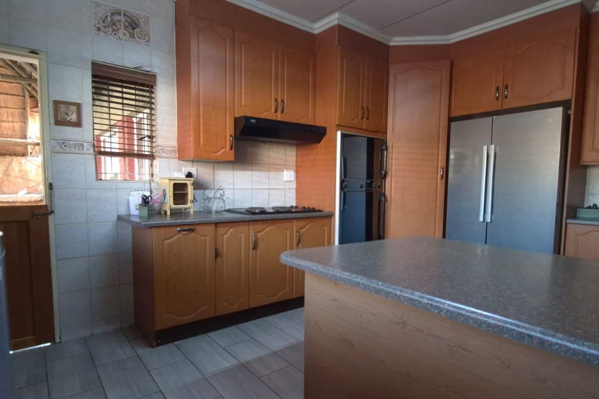 A functional kitchen featuring wooden cabinetry, laminate countertops, a central island, and tiled finishes, with direct access to an outdoor patio area.