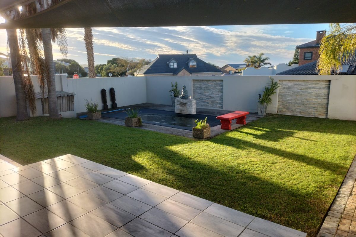 A well-maintained rear garden featuring a tiled patio, a small swimming pool with a cover, and perimeter boundary walls with stone cladding accents.