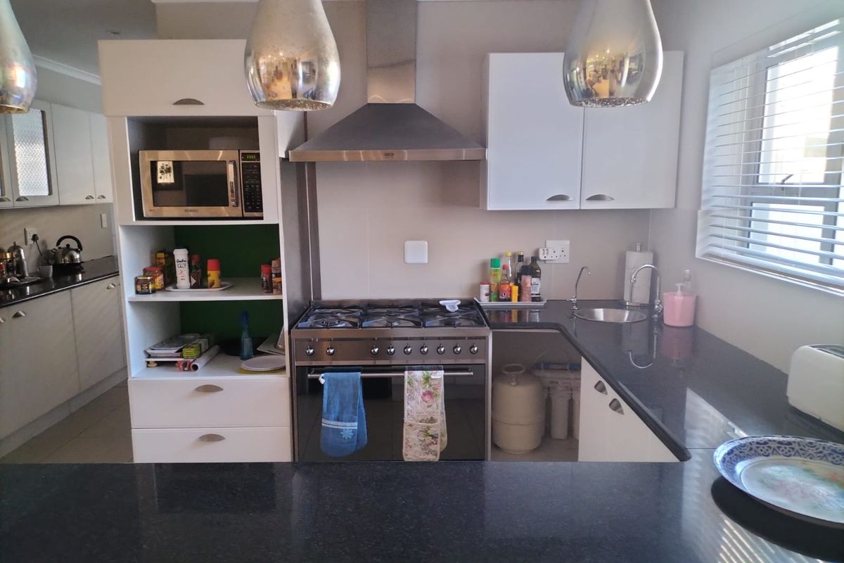 A functional kitchen featuring dark granite countertops, white cabinetry, a stainless steel gas stove with extractor fan, and a built-in microwave.