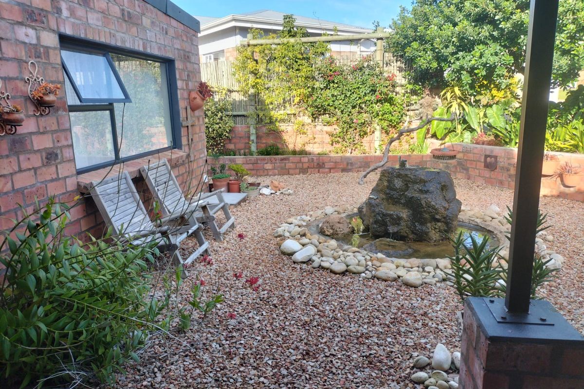 A landscaped rear garden featuring a stone water feature, gravel ground cover, and a brick-walled courtyard area.
