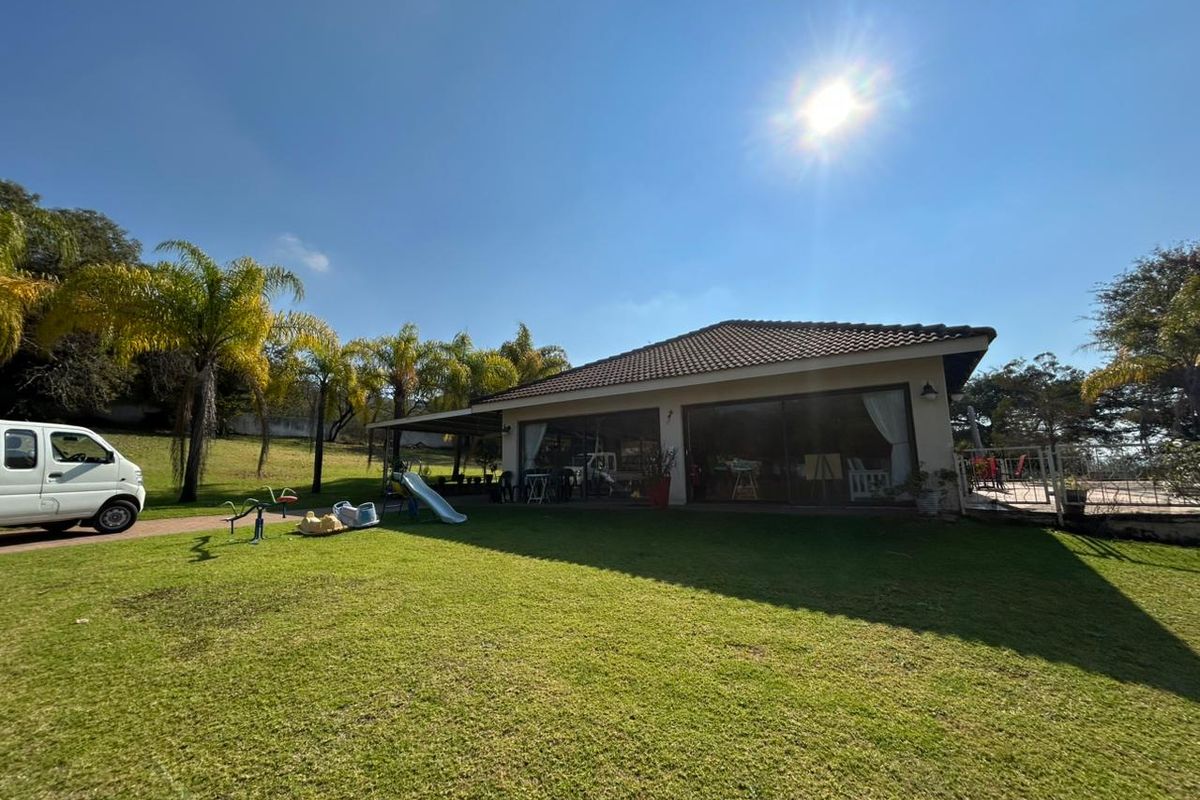 A view of the rear exterior of the farm property, featuring a spacious lawn, a covered patio area, and large sliding glass doors.