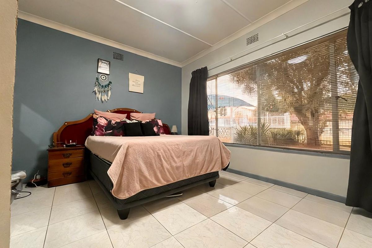 A bedroom featuring large format floor tiles, a feature wall, and a large window with integrated blinds.