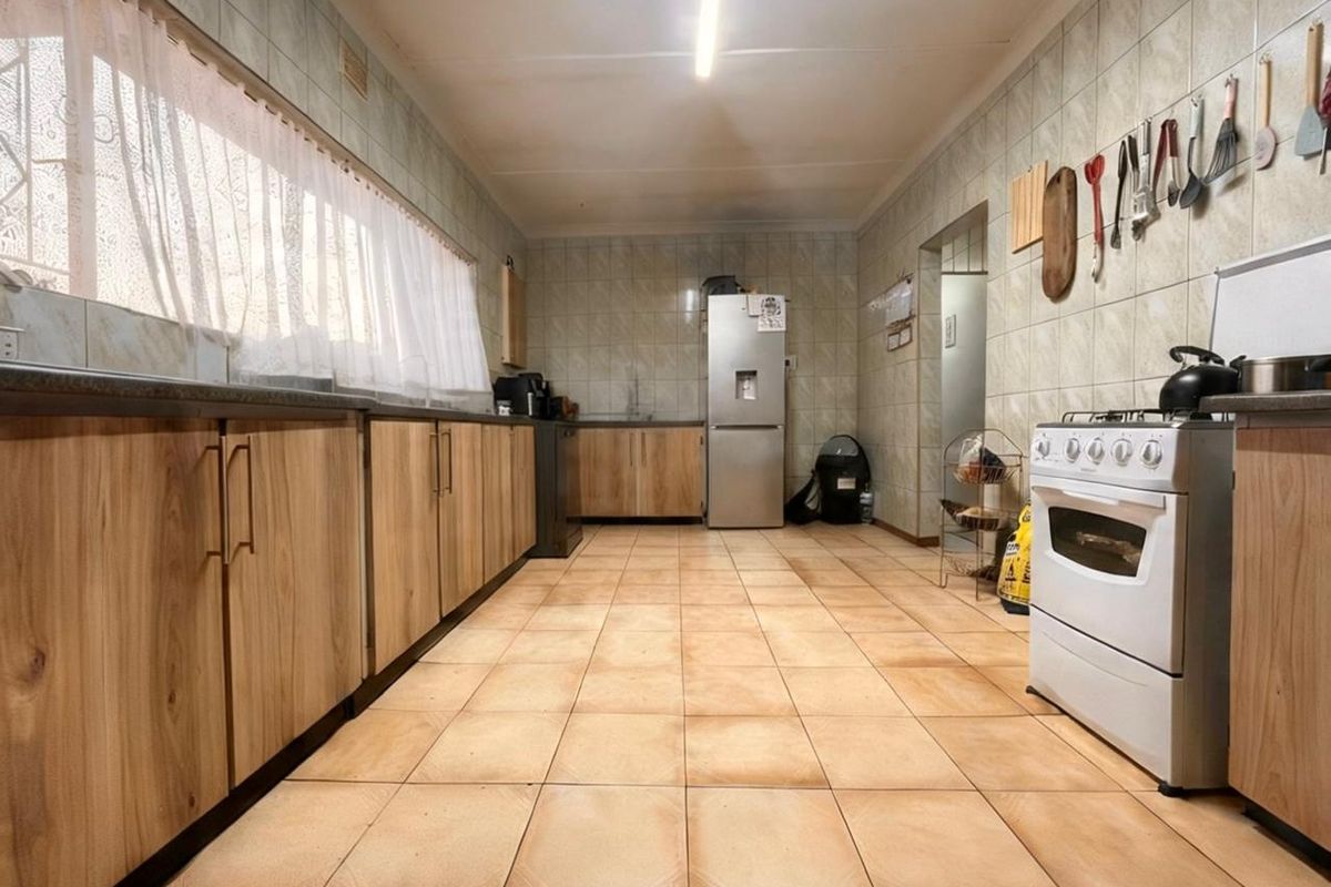 A functional kitchen featuring wood-look cabinetry, tiled flooring, and wall-mounted storage, providing a practical workspace with a freestanding stove.