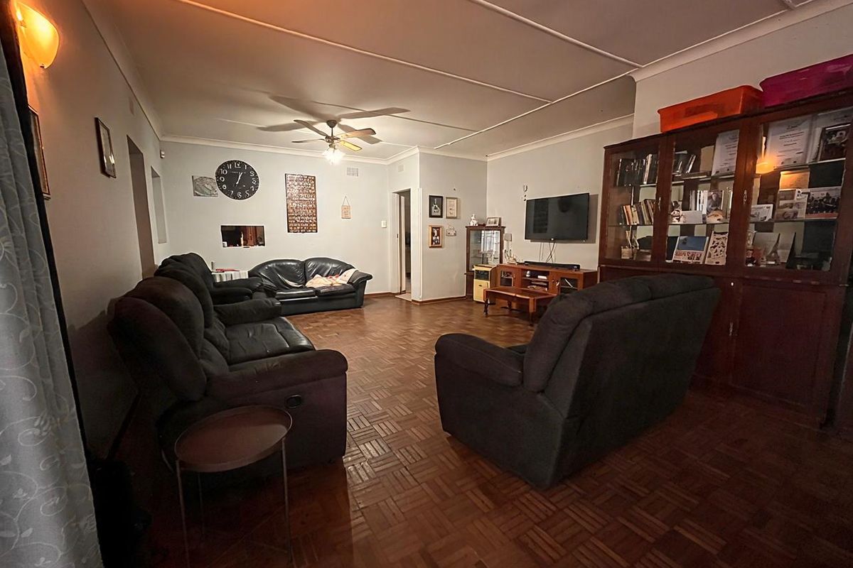 Spacious living room featuring traditional parquet flooring, a ceiling fan, and neutral wall finishes, providing a comfortable and functional family living space.