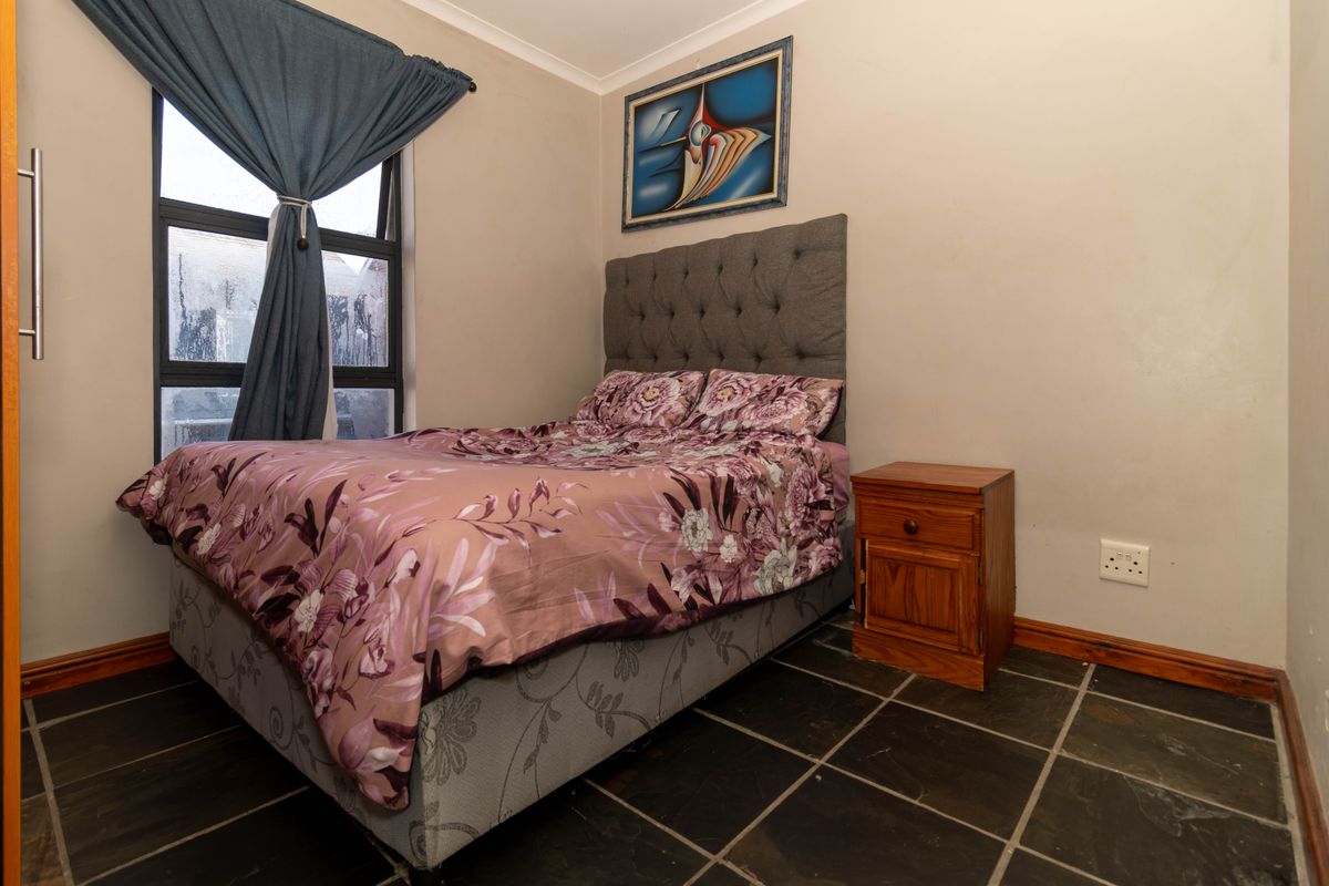 A compact bedroom featuring dark tiled flooring, a large window with curtaining, and neutral wall finishes.