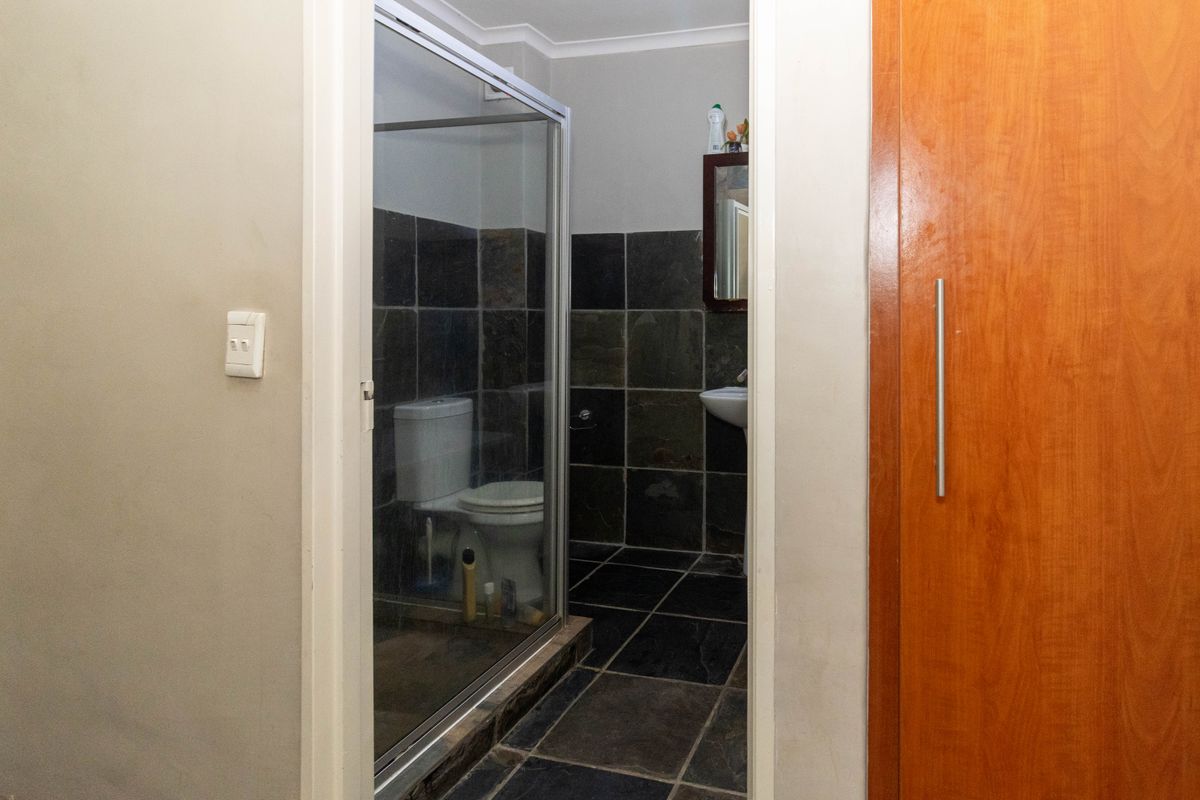 A compact bathroom featuring dark slate-style wall and floor tiles, a glass-enclosed shower, and a pedestal basin.