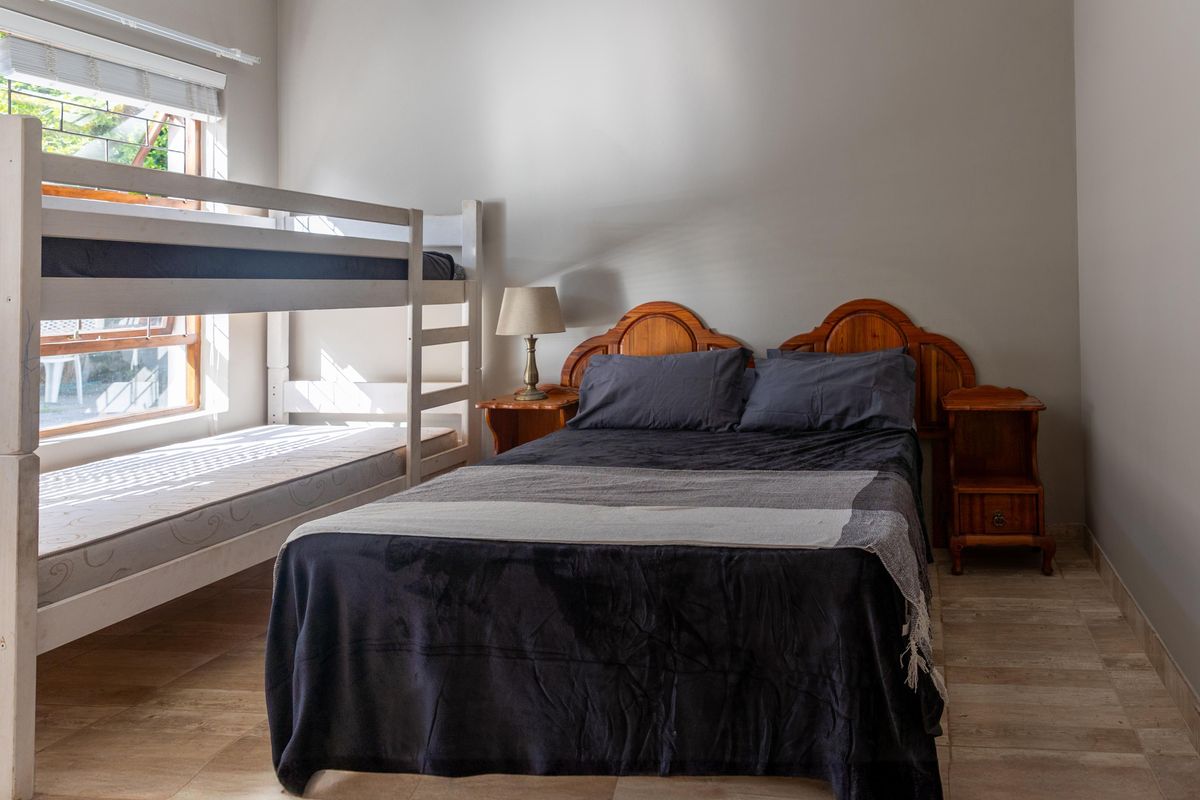 A functional bedroom featuring tiled flooring, a large window for natural light, and space for multiple beds.