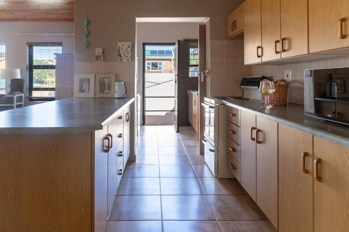 A functional kitchen featuring light wood cabinetry, tiled flooring, and a breakfast bar, with a direct view through to the rear exterior.