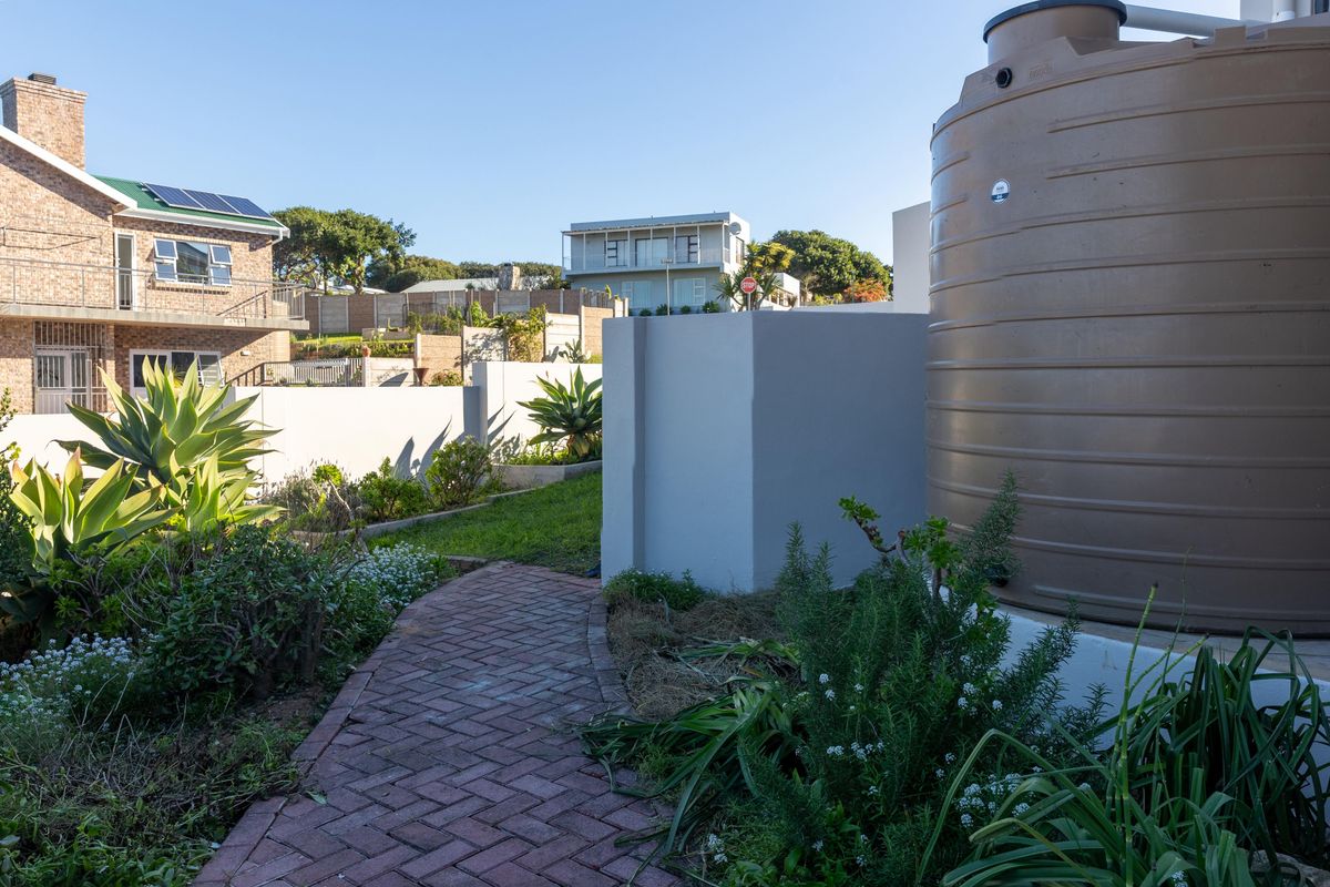 A well-maintained rear garden area featuring a paved walkway, landscaped garden beds, and a large water storage tank.