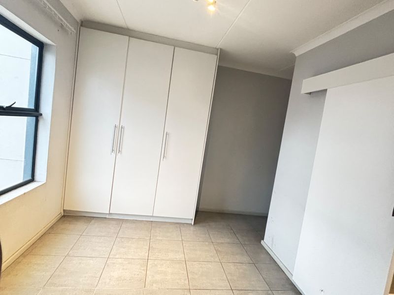 A clean, empty bedroom featuring neutral tiled flooring, built-in white cupboards, and a sliding door, offering a versatile space ready for personalization.
