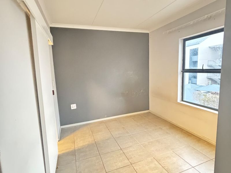 A bright, empty bedroom featuring neutral tiled flooring, a sliding door, and a large window with natural light.