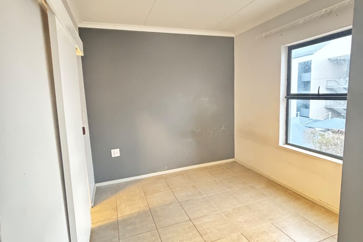 A bright, empty bedroom featuring neutral tiled flooring, a sliding door, and a large window with natural light.