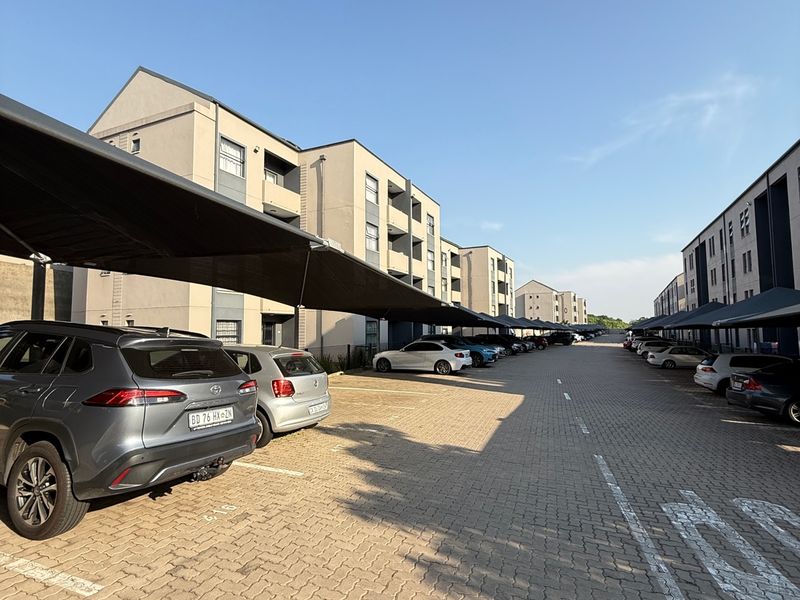 Exterior view of a modern apartment complex featuring paved parking areas with shade cloth carports for residents.