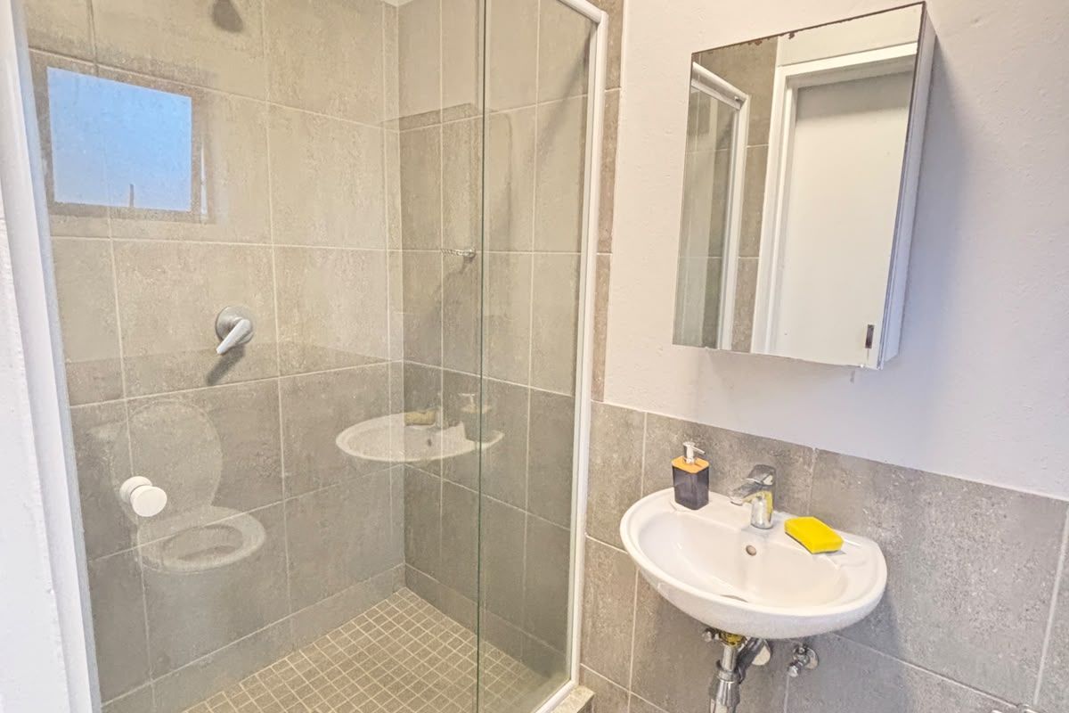 A clean, modern bathroom featuring a glass-enclosed shower, wall-mounted basin, and a mirrored medicine cabinet with neutral grey floor and wall tiling.