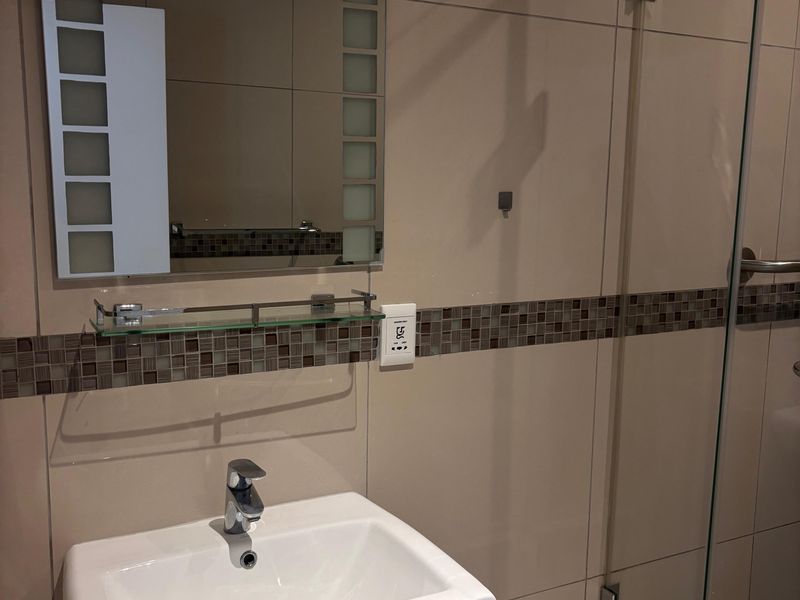 A modern bathroom featuring a pedestal basin, glass shower enclosure, and decorative mosaic tile accents on the wall.