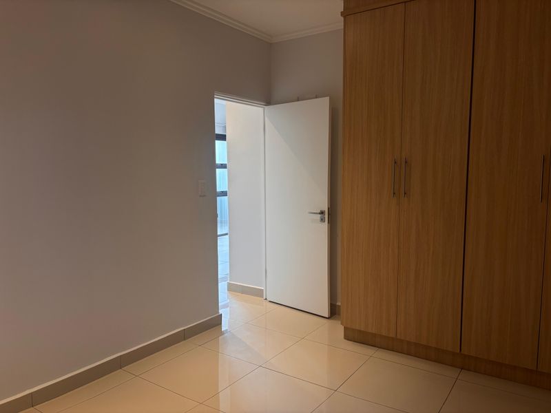 A clean bedroom interior featuring light-toned floor tiles and built-in wooden cabinetry with a modern door leading to an adjacent space.