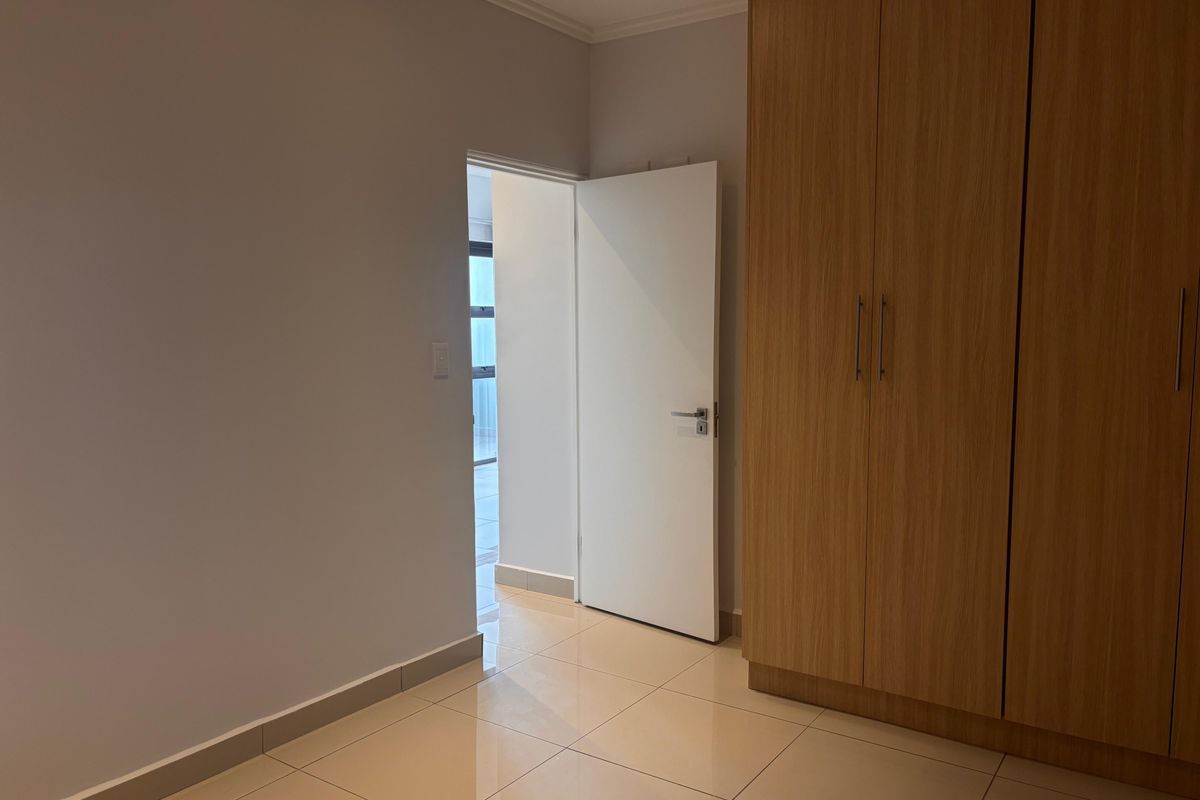 A clean bedroom interior featuring light-toned floor tiles and built-in wooden cabinetry with a modern door leading to an adjacent space.