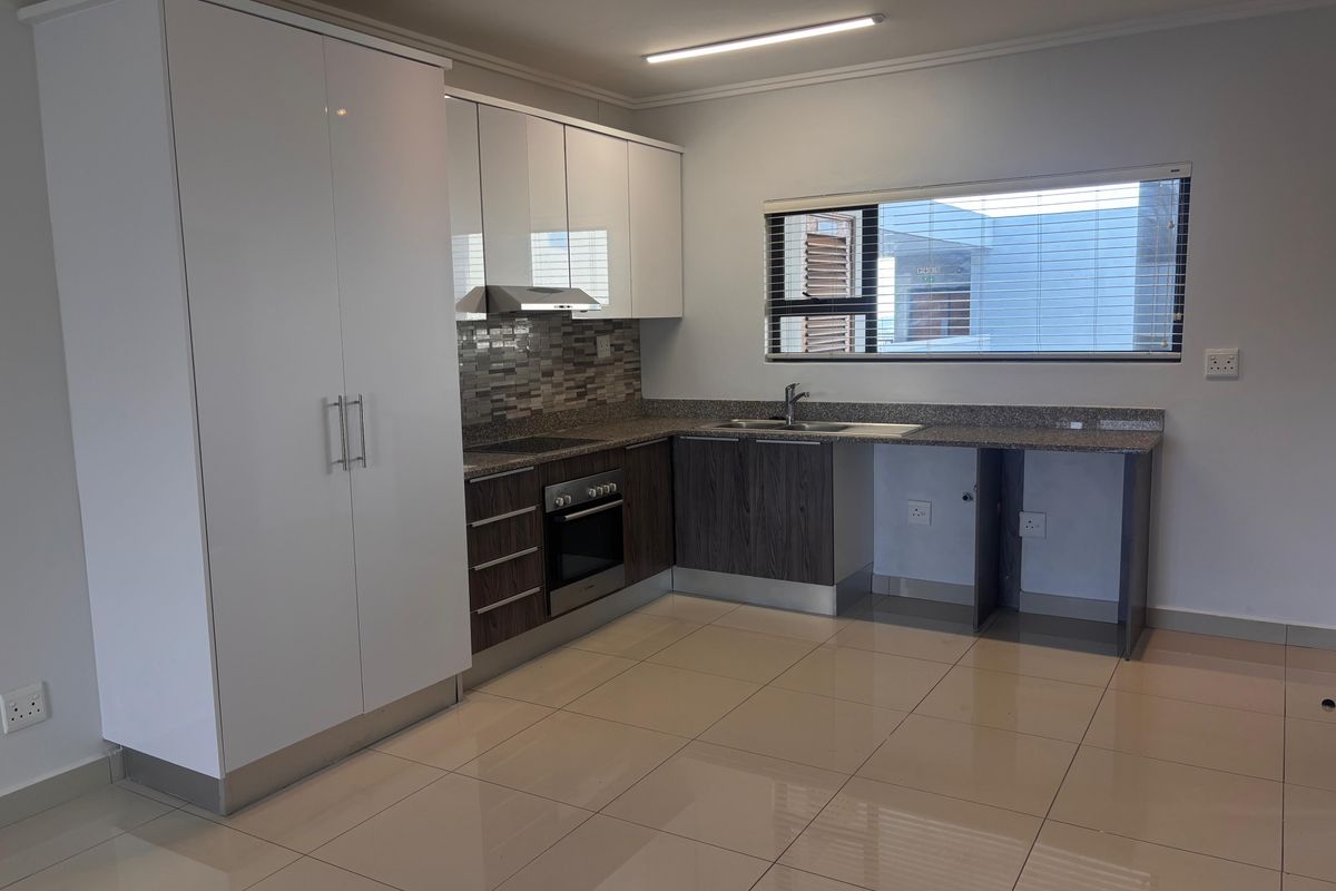 Modern kitchen featuring high-gloss white cabinetry, dark wood-finish lower cupboards, granite countertops, built-in oven, hob, extractor fan, and tiled flooring.