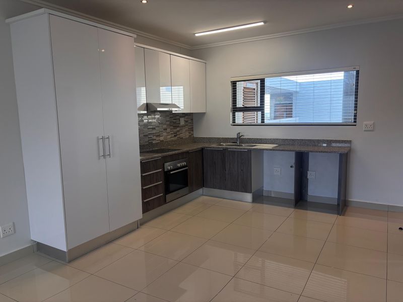 Modern kitchen featuring high-gloss white cabinetry, dark wood-finish lower cupboards, granite countertops, built-in oven, hob, extractor fan, and tiled flooring.
