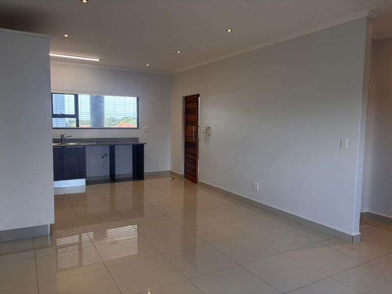 An open-plan living and kitchen area featuring tiled flooring, recessed lighting, and a compact kitchen counter with a sink.