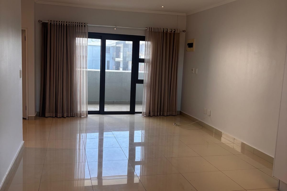 A spacious, empty living area featuring polished floor tiles, recessed downlighting, and sliding glass doors leading to a private balcony.