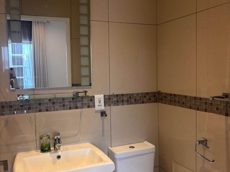 A modern bathroom featuring a pedestal sink, a white toilet, and full-height wall tiling with a decorative mosaic border.