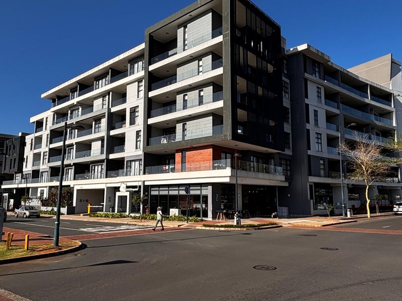 A modern multi-story apartment building featuring contemporary architectural design, glass balconies, and ground-floor commercial space, situated on a corner lot.