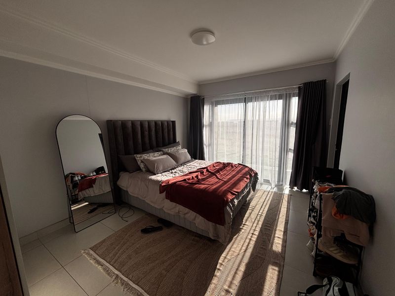 A well-lit bedroom featuring large sliding glass doors that provide natural light and access to an outdoor area, finished with neutral floor tiles.