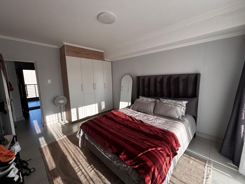 A well-lit bedroom featuring built-in wardrobes with overhead storage and tiled flooring, providing a clean and functional living space.