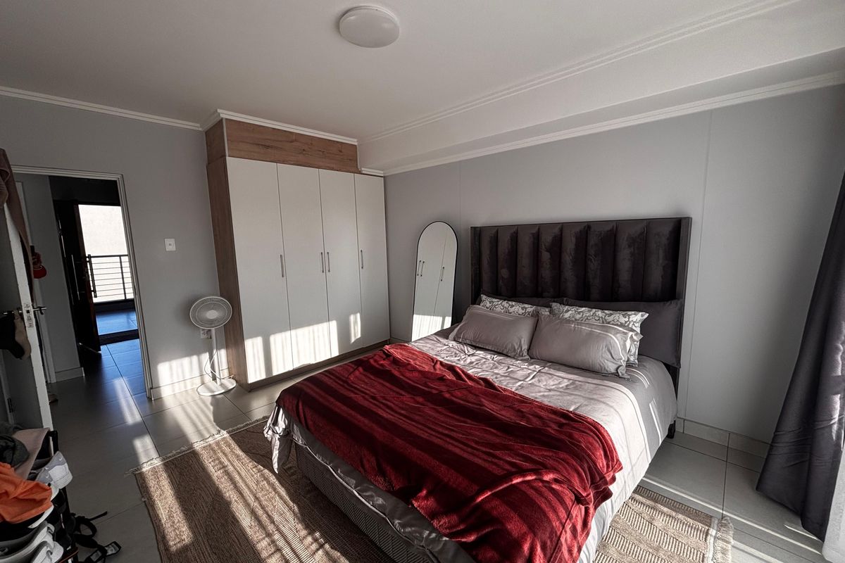 A well-lit bedroom featuring built-in wardrobes with overhead storage and tiled flooring, providing a clean and functional living space.