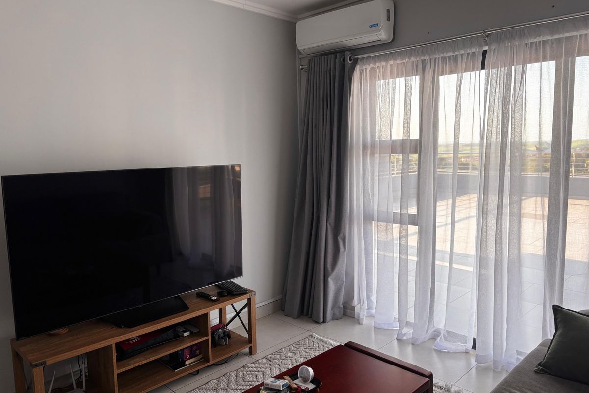 A bright living room featuring tiled flooring, a wall-mounted air conditioning unit, and large sliding glass doors providing access to an outdoor balcony.