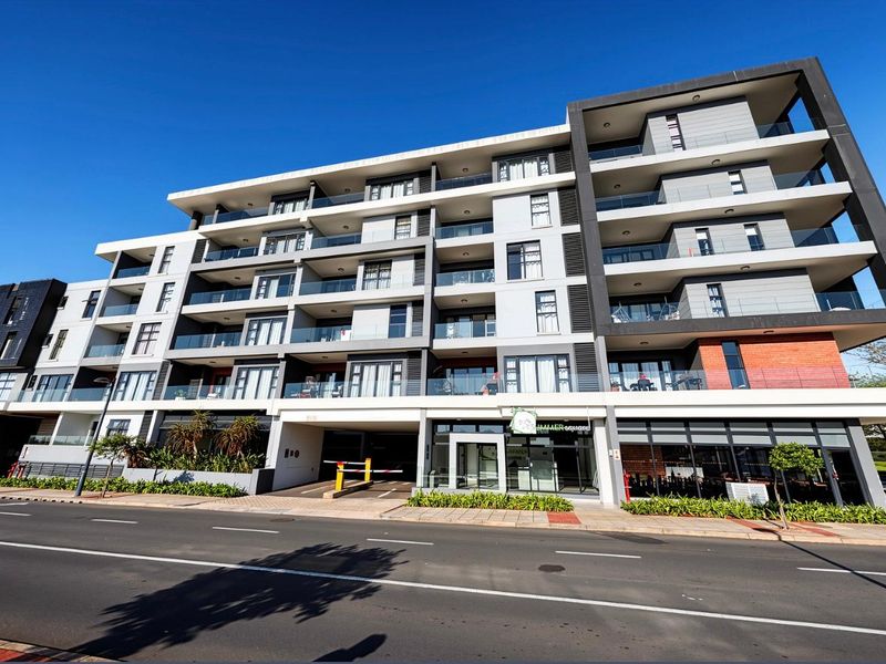 Modern multi-story apartment complex featuring contemporary architectural design, glass-fronted balconies, and ground-level commercial access with secure parking entrance.