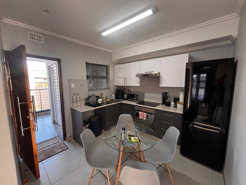 Modern open-plan kitchen featuring sleek cabinetry, stone countertops, built-in oven, hob, and extractor fan, with direct access to a private balcony.