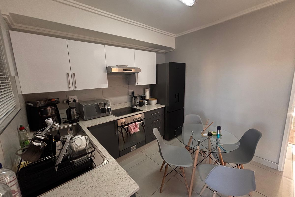 A compact, modern kitchen featuring white upper cabinetry, dark lower cabinets, stone-look countertops, and a built-in oven with an extractor fan.