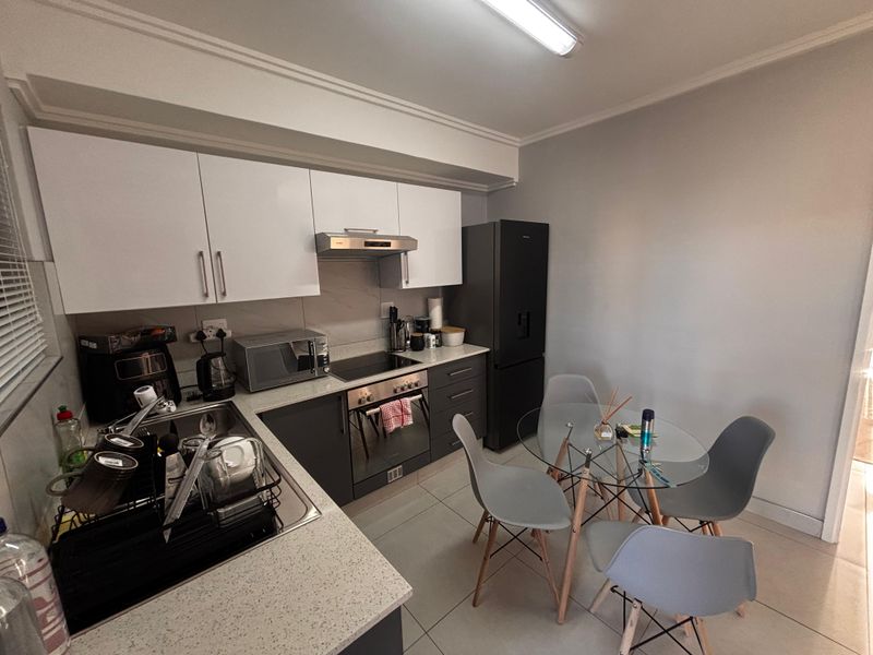 A compact, modern kitchen featuring white upper cabinetry, dark lower cabinets, stone-look countertops, and a built-in oven with an extractor fan.